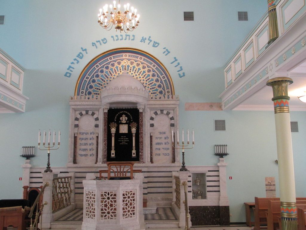 Intérieur de la synagogue de Peitav avec ses murs blancs et menoroth qui entourent la tevah